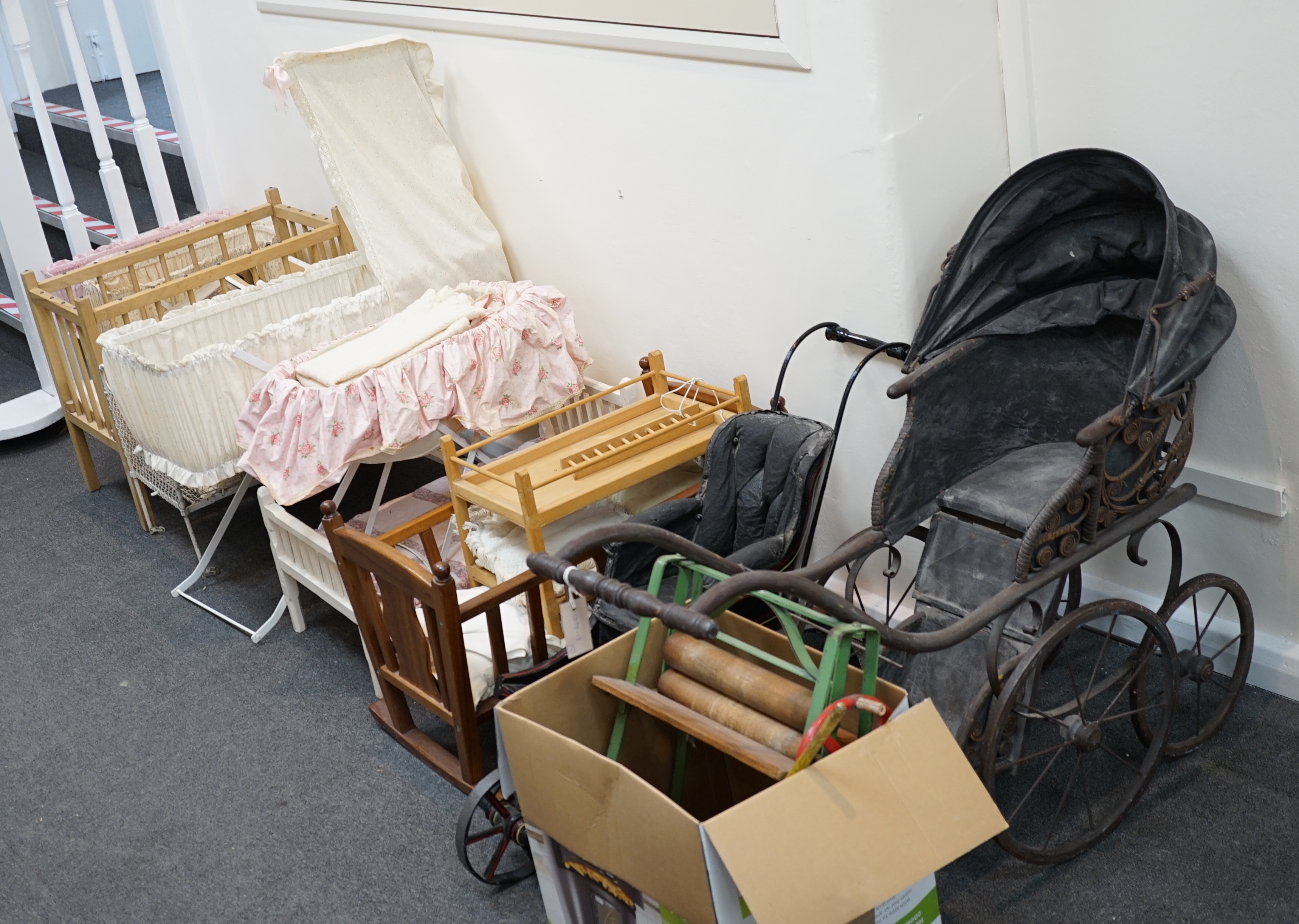 A collection of nine doll’s cribs of wood or wrought iron construction, together with two nineteenth century style doll’s ’bath chairs’, a toy mangle, Disney themed Snow White carpet sweeper and a boxed child’s sewing ma